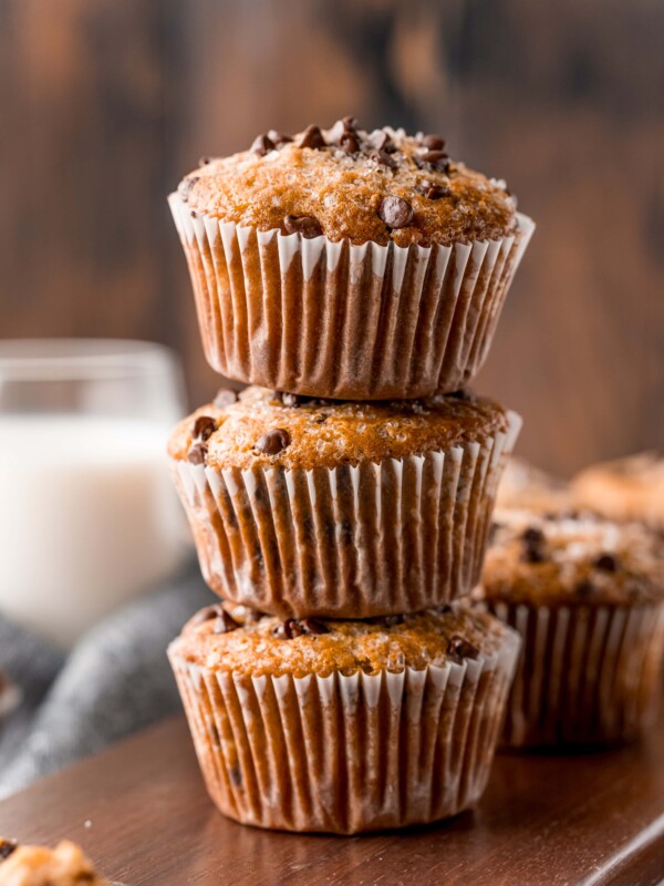 A stack of delicious chocolate chip muffins on a rustic wooden cutting board.