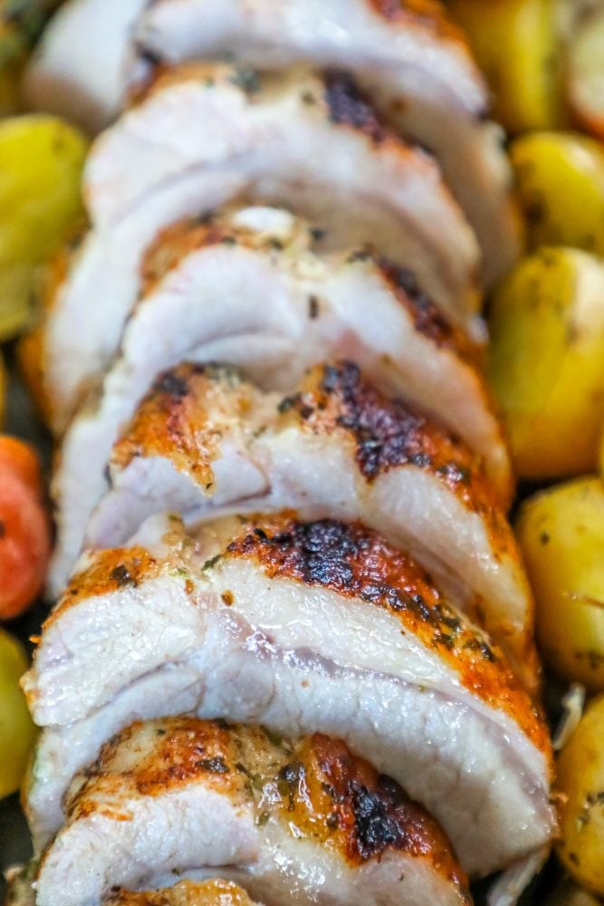 picture of baked pork loin in a pan with seasoned potatoes and onions and a sprig of rosemary