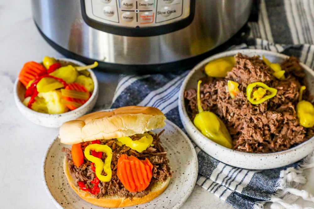 picture of shredded Italian beef in a bun on a plate in front of an Instant Pot