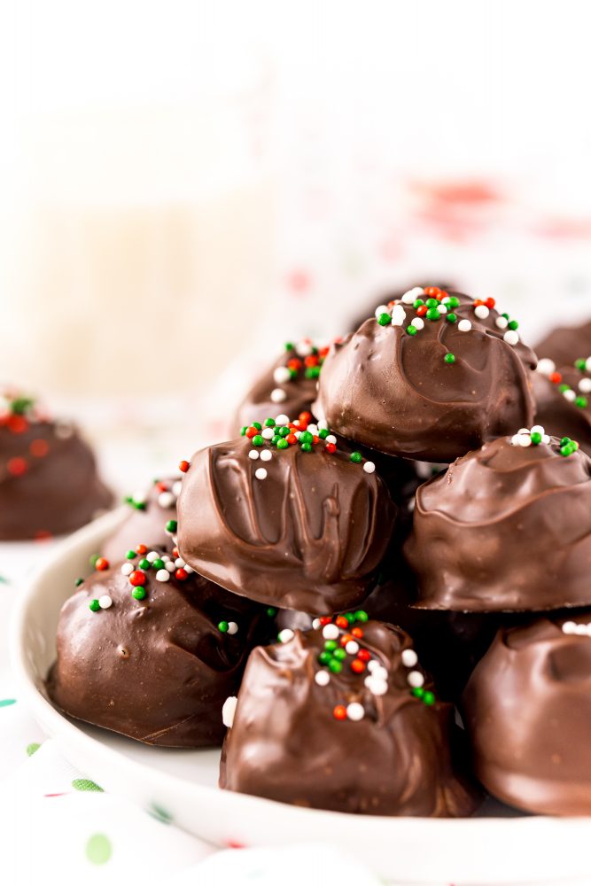 chocolate covered buttercream candy balls with green, white, and red sprinkles on top stacked on top of each other on a white plate