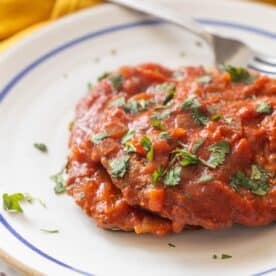 A plate of enchiladas topped with red sauce, reminiscent of a tomato Swiss Steak recipe, and garnished with chopped cilantro, sits invitingly with a fork beside the food.