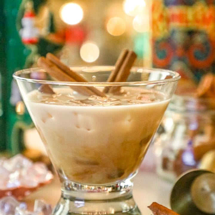 A martini glass with cinnamon sticks and a bottle of caramel vodka.