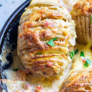 Creamy stuffed hasselback potatoes cooked in a skillet with a wooden spoon.