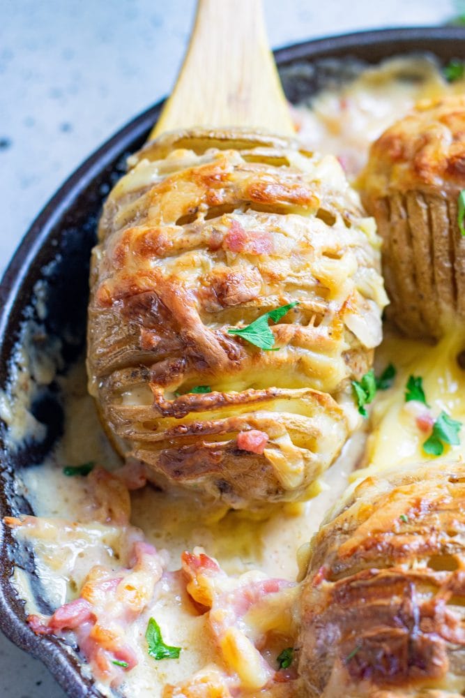 hasselback potatoes in gratin sauce in a cast iron skillet one on a wooden spoon.