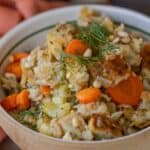 A bowl of vegetable casserole with carrots, cauliflower, and pine nuts, featuring a hint of Greek flavored stuffing recipe and garnished with fresh dill.