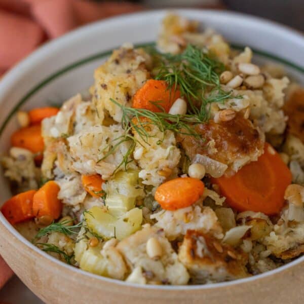 A bowl of vegetable casserole with carrots, cauliflower, and pine nuts, featuring a hint of Greek flavored stuffing recipe and garnished with fresh dill.