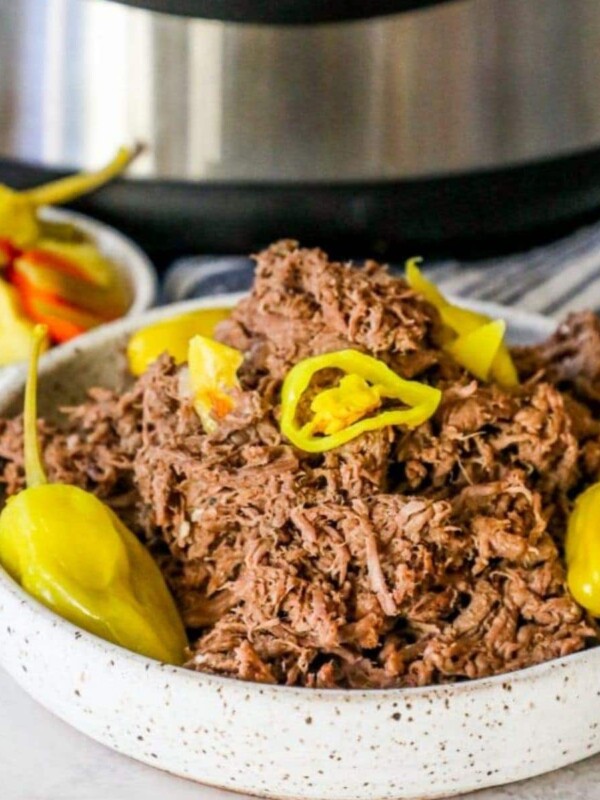 picture of shredded italian beef with banana pepper rings and pepperoncini pepper in front of an Instant pot