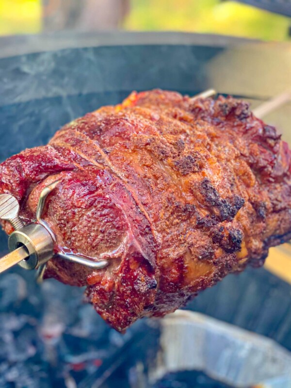 A prime rib being grilled on a rotisserie.
