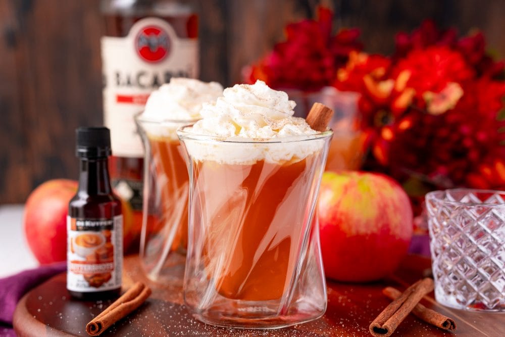 butter rum cider in a glass with whipped cream and cinnamon sticks