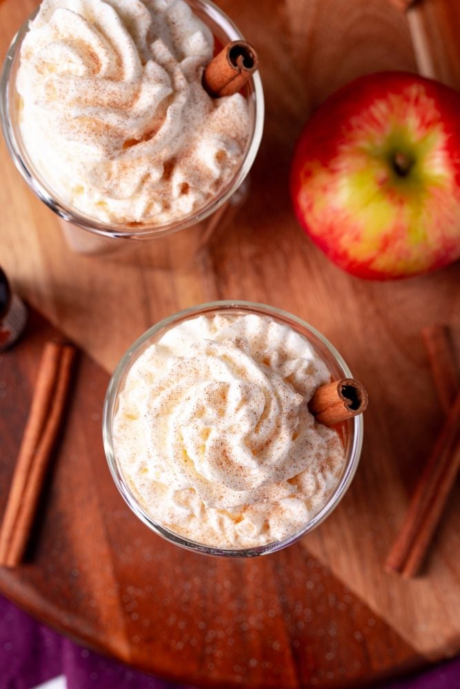 butter rum cider in a glass with whipped cream and cinnamon sticks