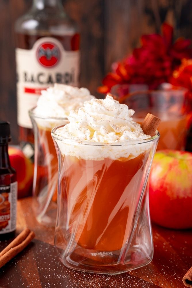 butter rum cider in a glass with whipped cream and cinnamon sticks