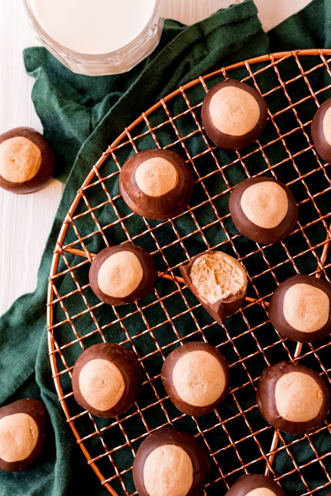 keto peanut butter balls dipped in chocolate on a wire rack, one with a bite taken out of it