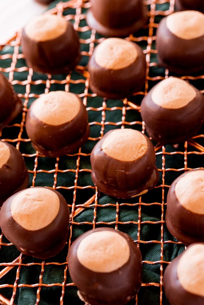 keto peanut butter balls dipped in chocolate on a wire rack, over a green tea towel 