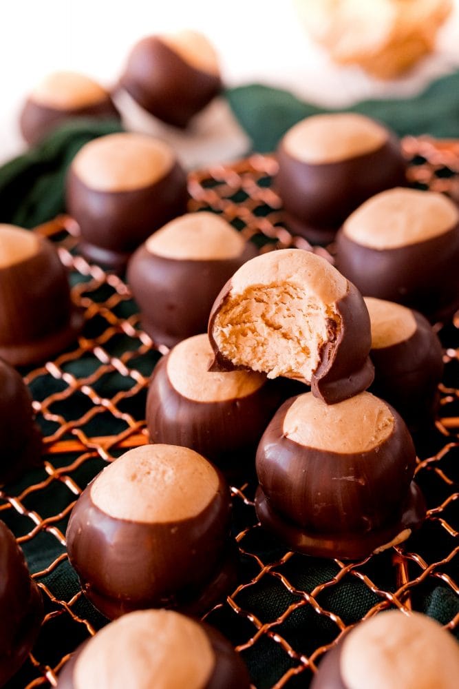 keto peanut butter balls dipped in chocolate on a wire rack, one with a bite taken out of it