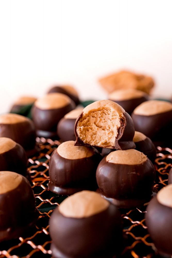 keto peanut butter balls dipped in chocolate on a wire rack, one with a bite taken out of it