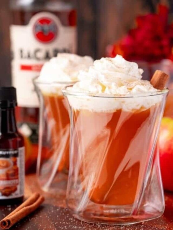Two glasses of apple cider with whipped cream and cinnamon.