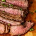 Sliced medium-rare broiled top round steak garnished with chopped green onions on a wooden cutting board—an easy London broil perfect for any occasion.