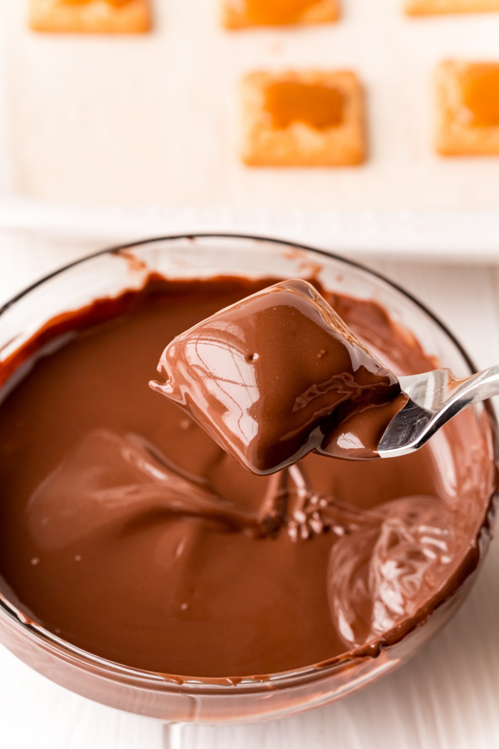 A spoon is dipping chocolate into a bowl of crackers for an easy millionaire shortbread bites recipe.