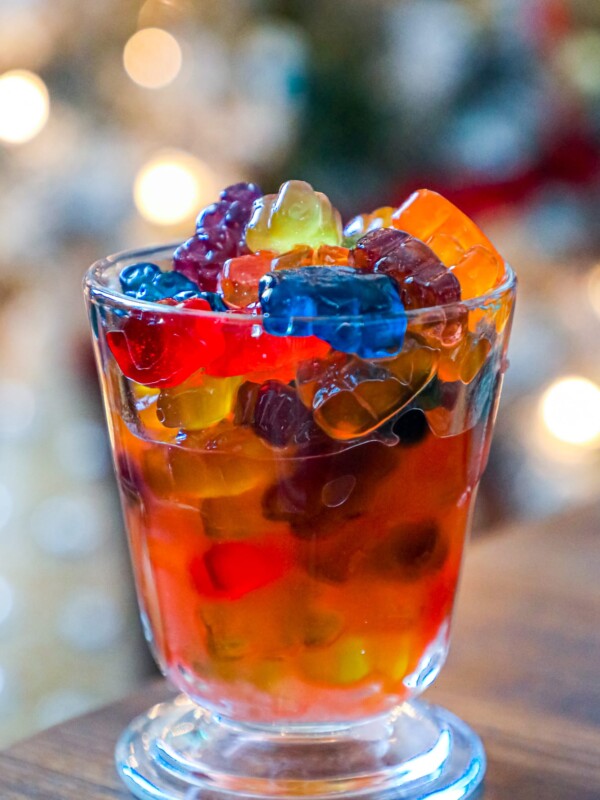 Boozy Negroni gummy bears in a glass with a Christmas tree in the background.