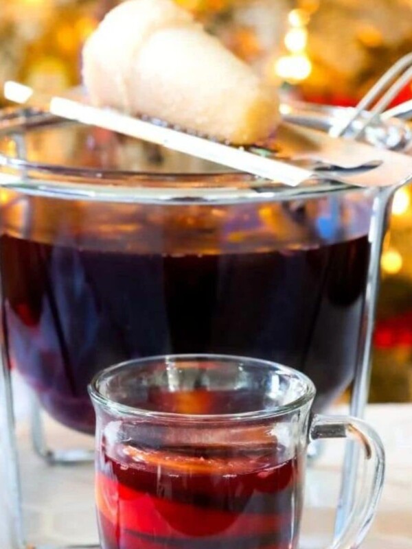 Feuerzangenbowle in a mug in front of a punch bowl with a sugar cone on fire over it