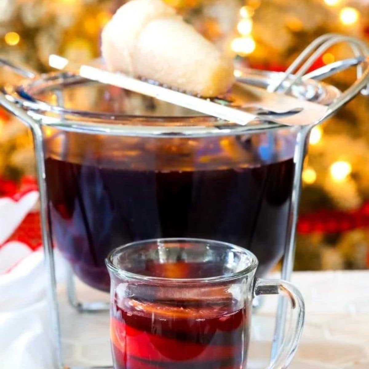 Feuerzangenbowle in a mug in front of a punch bowl with a sugar cone on fire over it