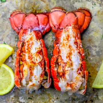broiled lobster tails on a baking sheet with lemon slices next to them