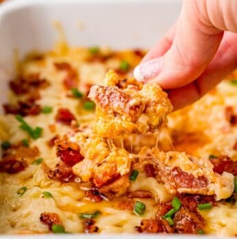 A person preparing a savory bacon and cheese dip by dipping a piece of bacon and cheese casserole into a dish.