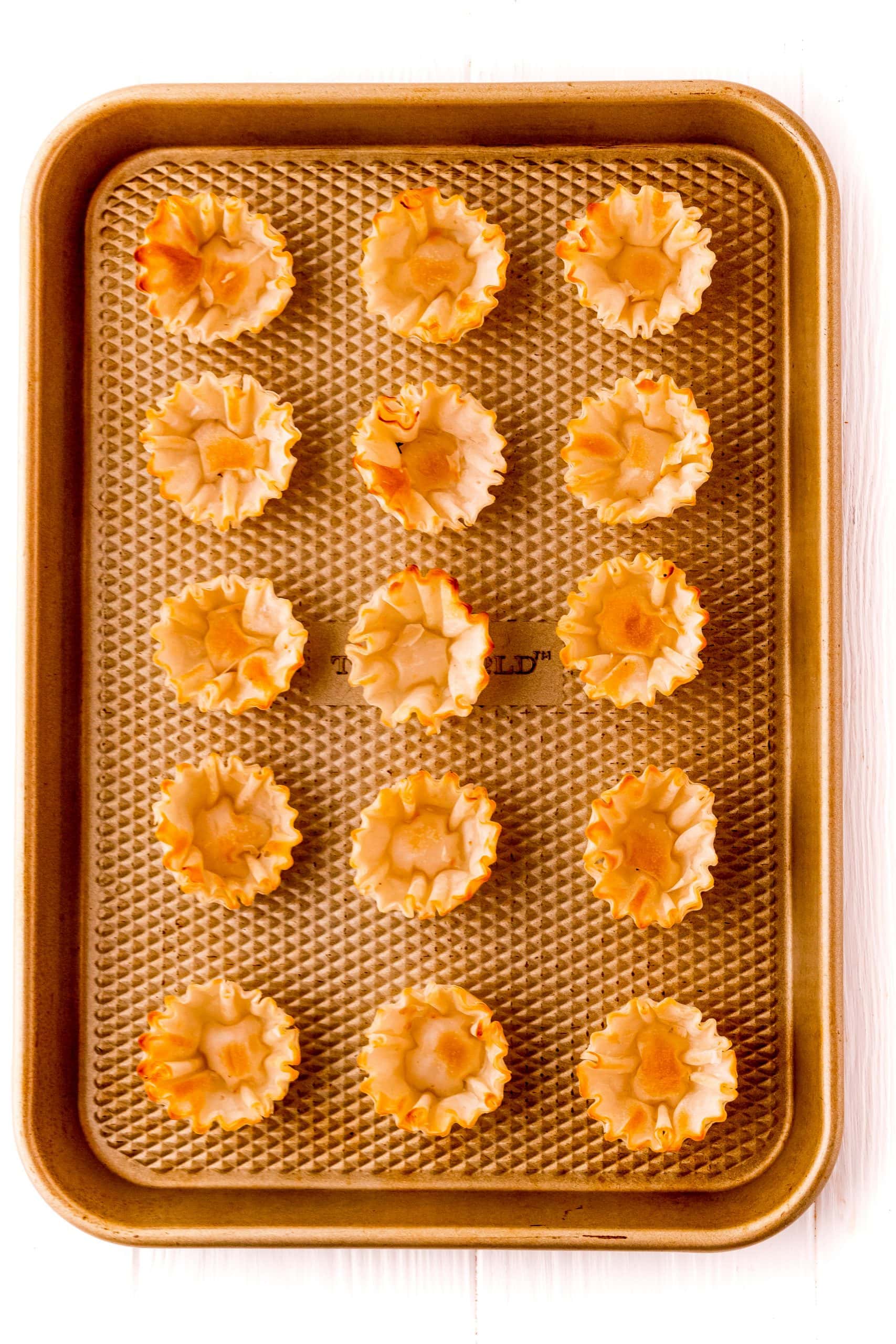 A baking sheet laden with mini phyllo tarts, prepped and ready for the oven, featuring raspberry and cheese fillings.