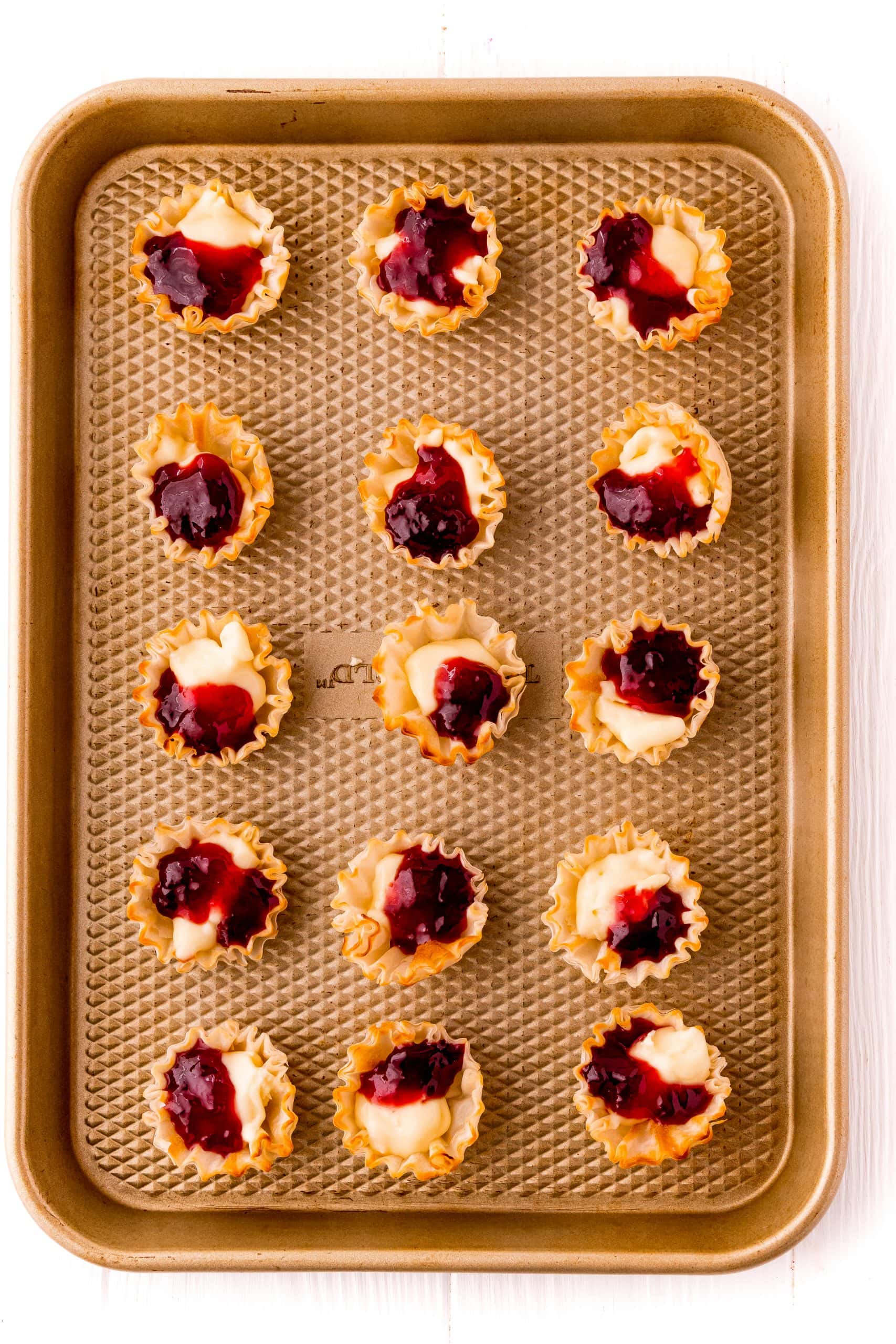 A tray of mini tarts, beautifully arranged and glistening with a sweet cranberry sauce topping, waiting to be served.