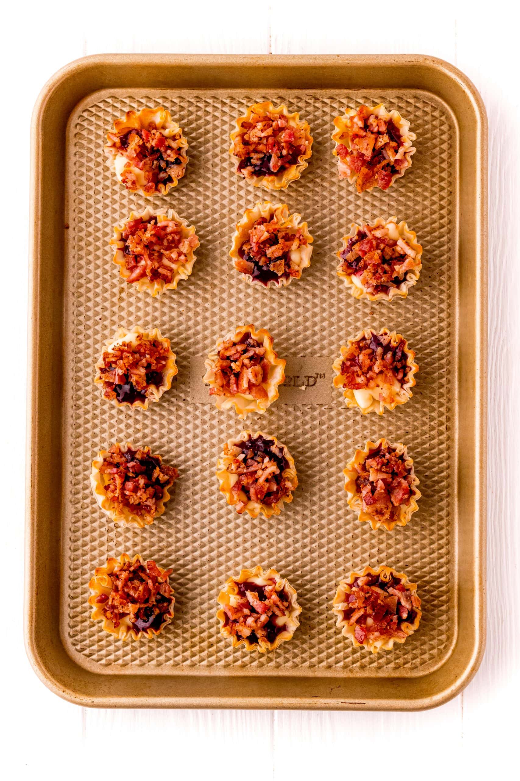 A baking sheet filled with an array of small, delectable bites featuring bacon and raspberry cheese, ready to be enjoyed.