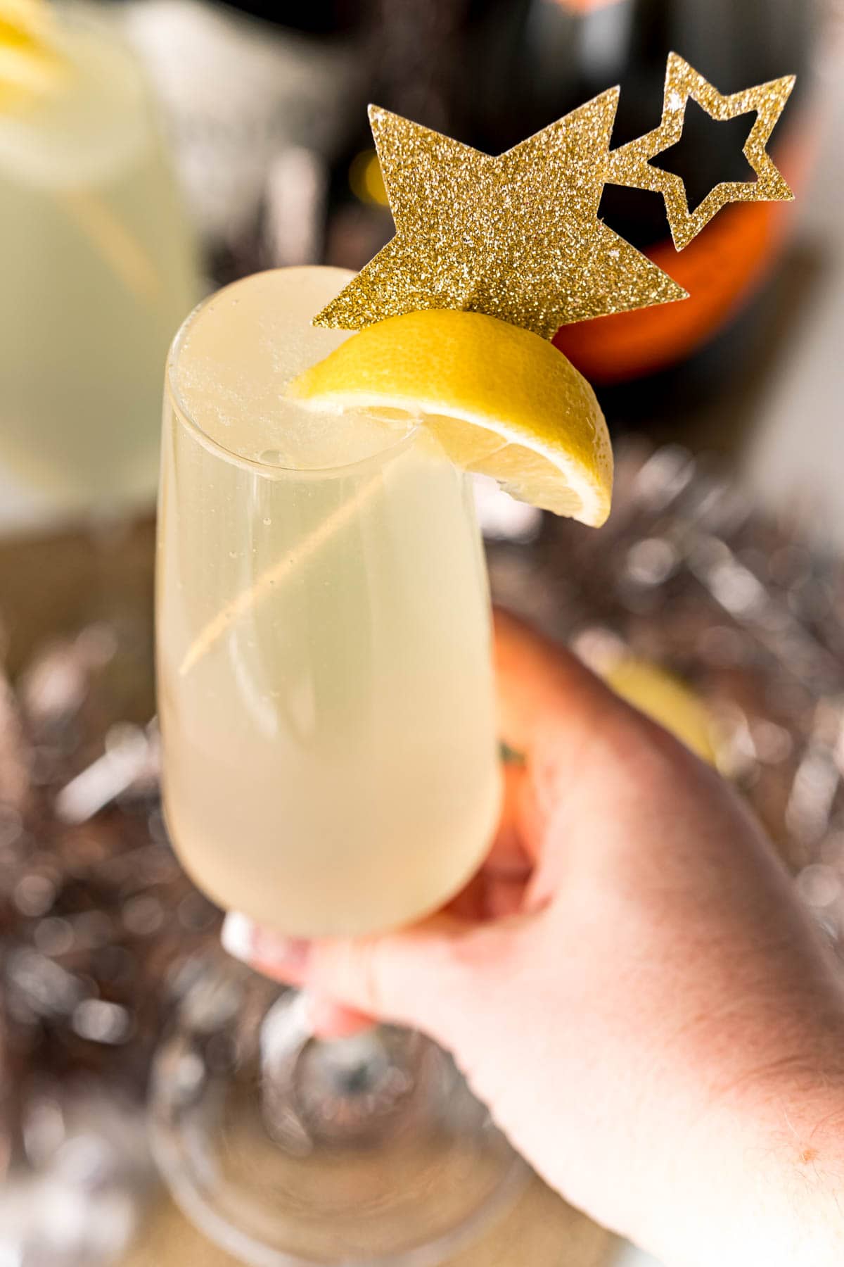 A person holding a glass of Champagne with a star garnish, enjoying an Easy Champagne Gin Fizz Cocktail.