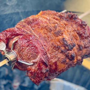 Close-up of a Kamado Joe prime rib with a crispy, browned exterior, mounted on a metal skewer.