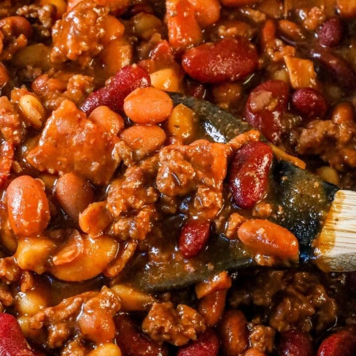 A bowl of the best ever slow cooker bean bake, served with a wooden spoon.