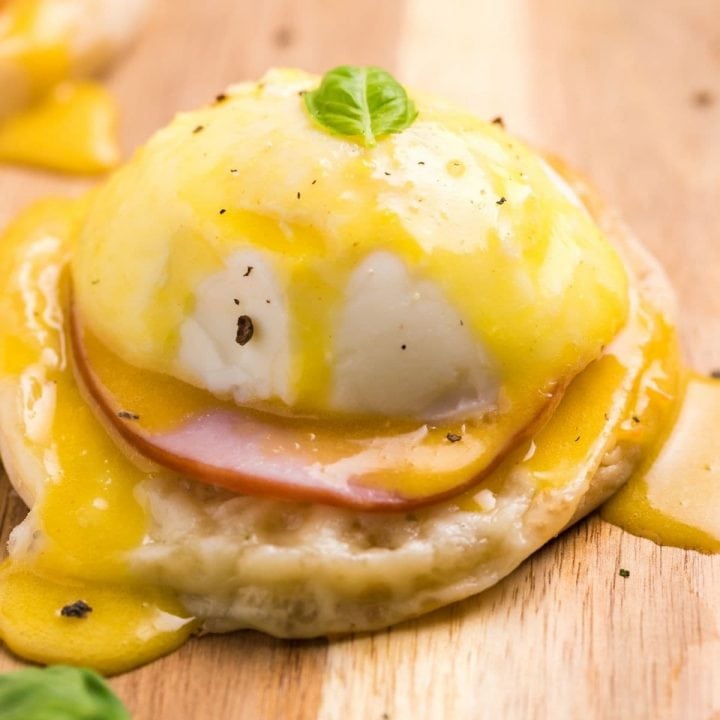 Easy Eggs Benedict recipe with ham and hollandaise sauce on a wooden cutting board.
