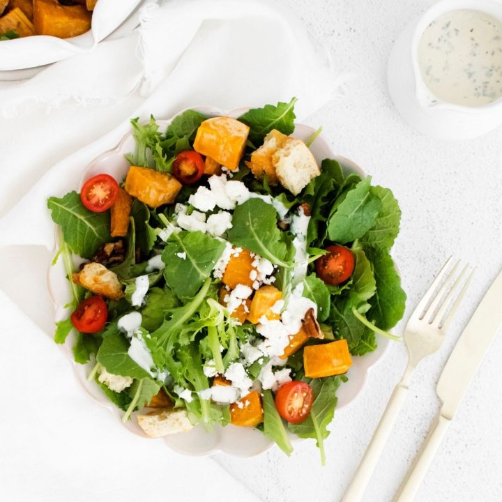 A plate with a Roasted Sweet Potato and Goat Cheese salad and dressing on it.