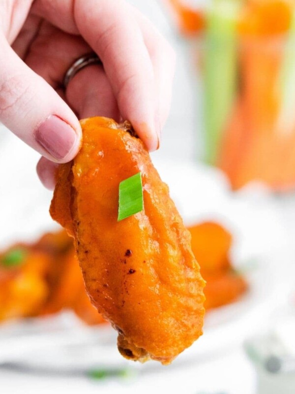 A person holds a plate of honey buffalo chicken wings with carrots and celery.