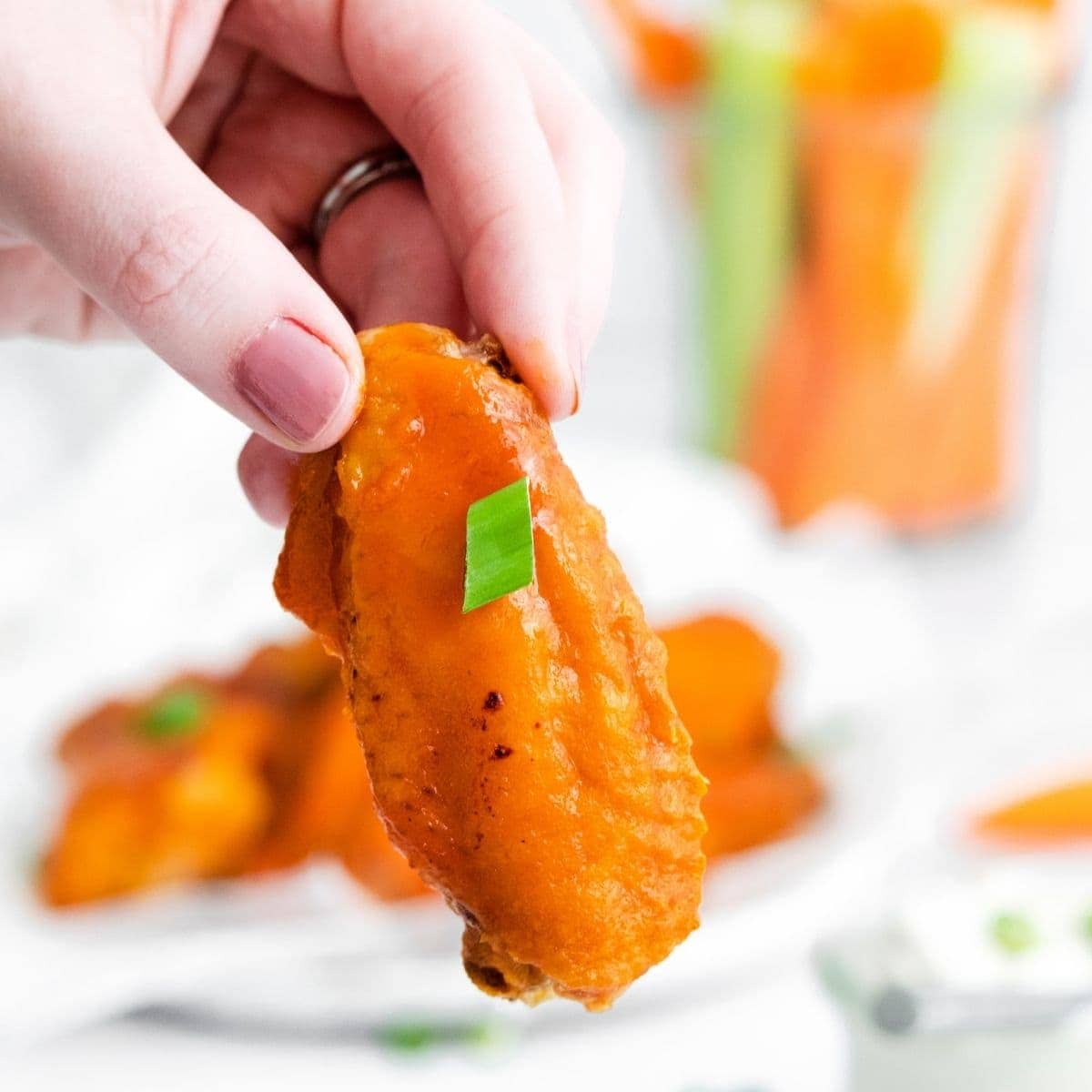 A person holds a plate of honey buffalo chicken wings with carrots and celery.