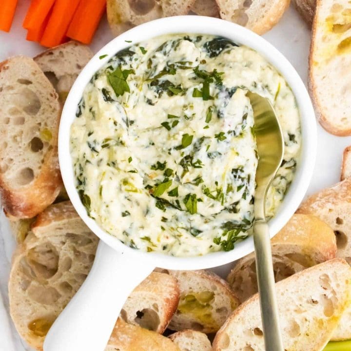 spinach dip in a white bowl with bread and crackers