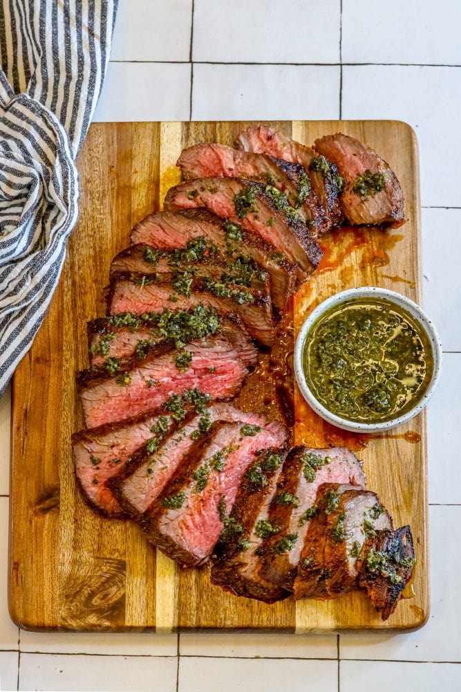 picture of sliced tri tip steak on a cutting board with chimichurri sauce on top 