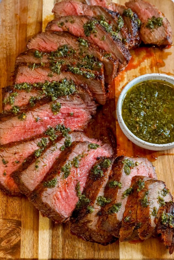 picture of sliced tri tip steak on a cutting board with chimichurri sauce on top 