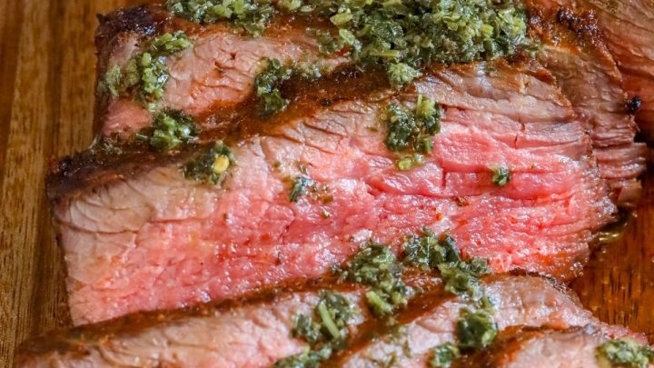 picture of sliced tri tip steak on a cutting board with chimichurri sauce on top