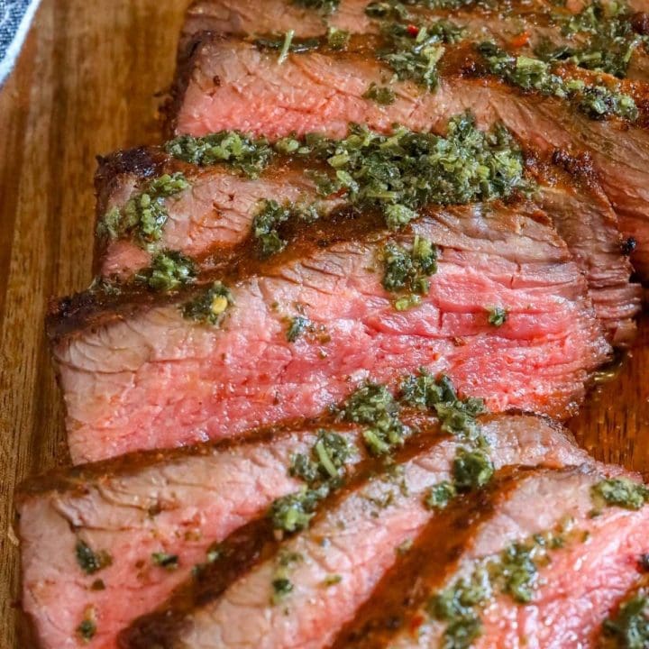 picture of sliced tri tip steak on a cutting board with chimichurri sauce on top