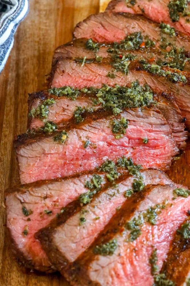 picture of sliced tri tip steak on a cutting board with chimichurri sauce on top 