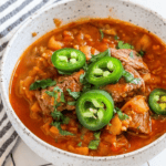 Steak green chili in a bowl with jalapenos.