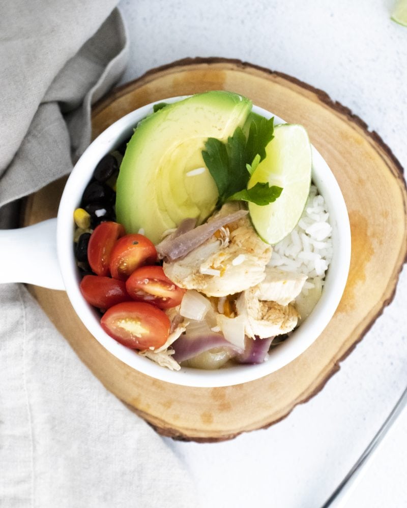 chicken, sliced avocados, sliced tomatoes, rice, and a slice of lime in a bowl on a table