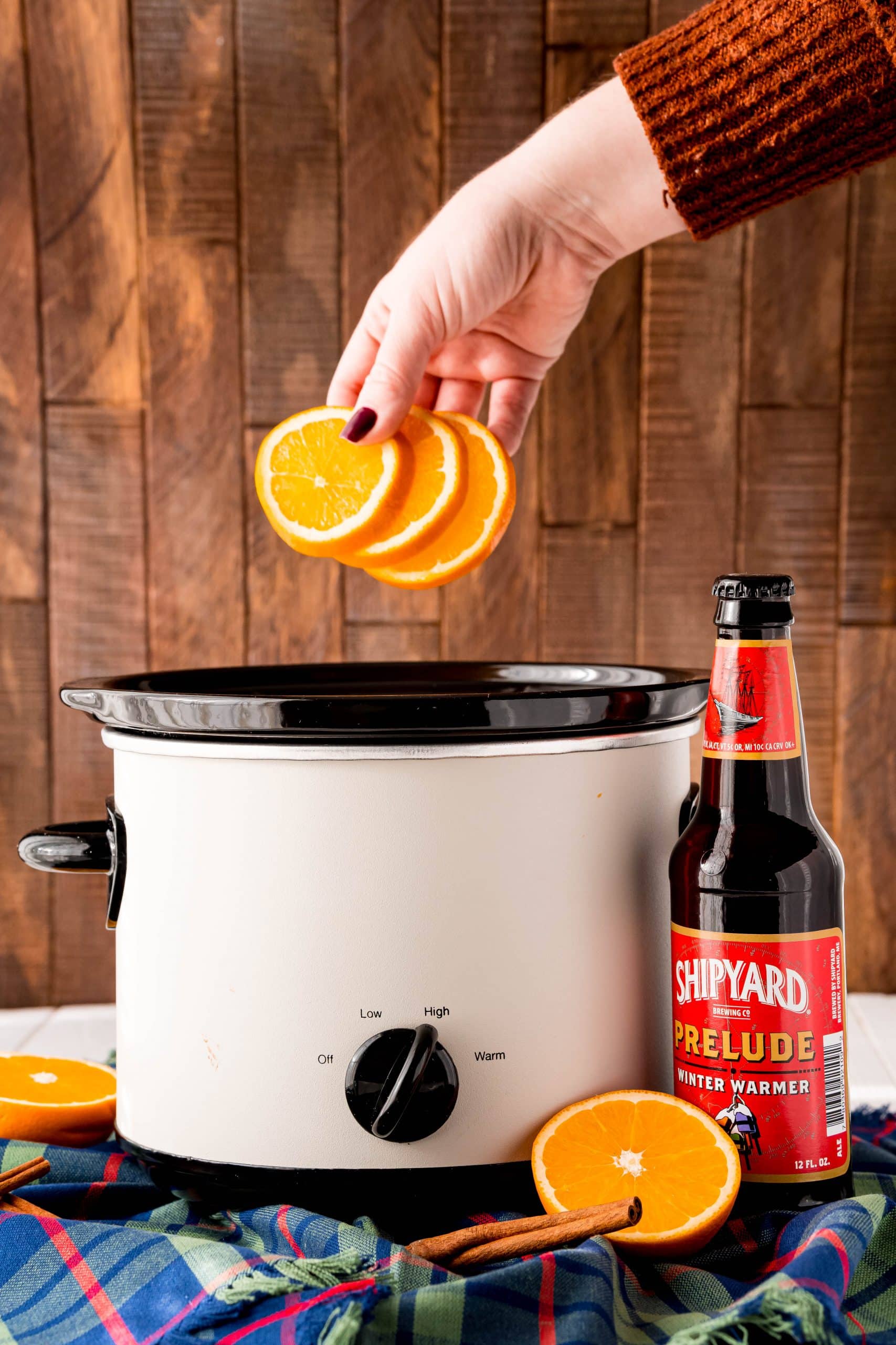 a hand putting slices of oranges into slow cooker