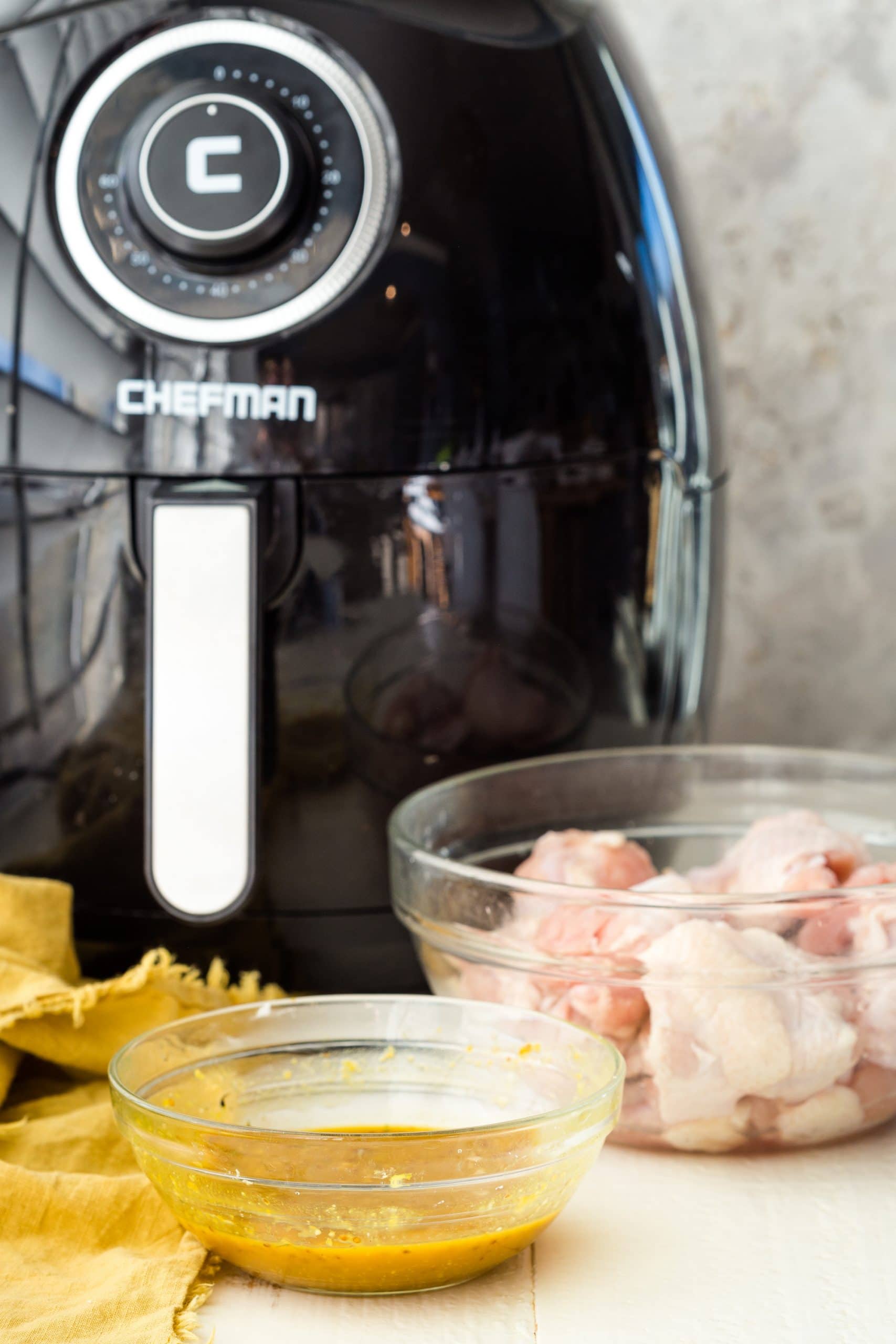 air fryer in the background with bowl of raw wings and sauce