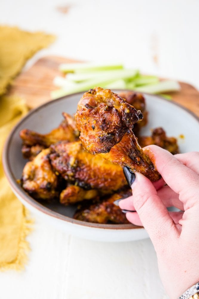 sticky wings on a plate, one being held up