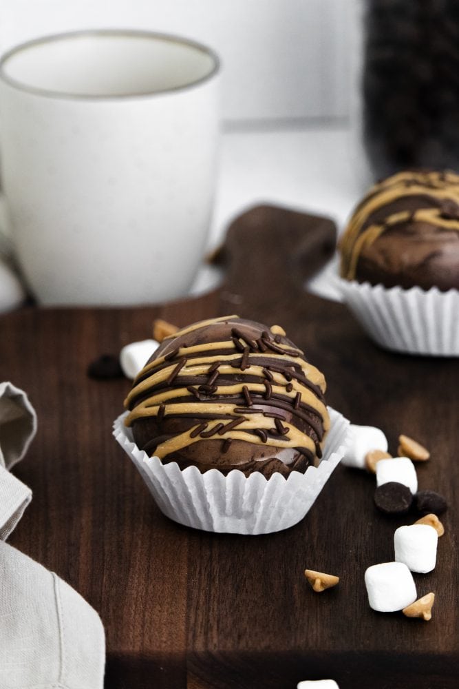 peanut butter hot chocolate bombs with peanut butter and chocolate sprinkles, marshmallows in the background.