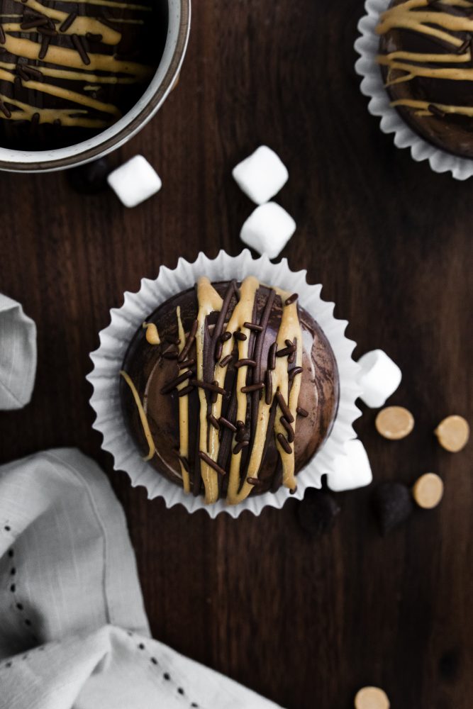 peanut butter hot chocolate bombs with peanut butter and chocolate sprinkles, marshmallows in the background.